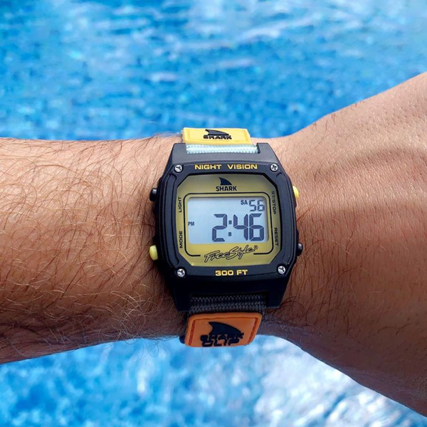 A Freestyle SHARK CLASSIC CLIP TURQ/BLK/MUSTARD watch stands out above a blue swimming pool.