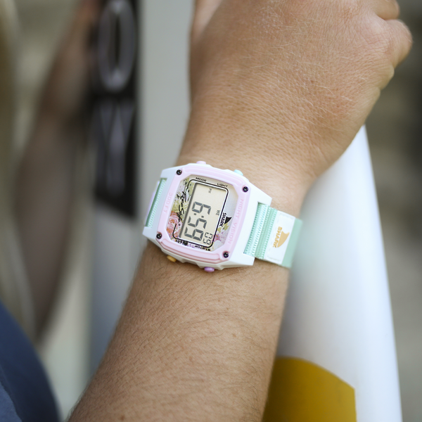 A person wears a Freestyle SHARK CLASSIC CLIP MINT BLUSH watch with a pastel strap, its digital display visible.