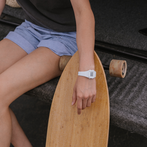 Person in shorts wearing a Freestyle SHARK MINI WHITE OUT watch, sitting on a ledge and holding a longboard.