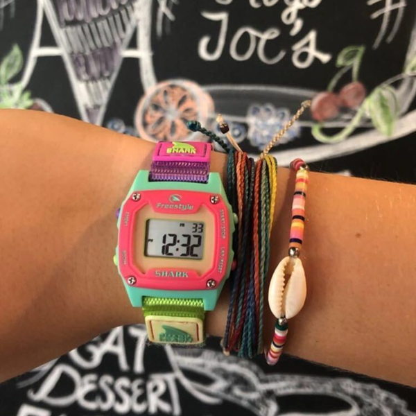Freestyles SHARK MINI LEASH SOUR APPLE watch and bracelets on a wrist in front of a chalkboard.