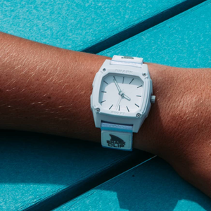 A Freestyle SHARK CLASSIC CLIP ANALOG WHITE WATER watch rests on a bright turquoise surface.