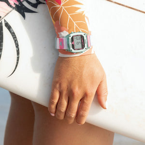 Wearing a Freestyle CAROLINE MARKS SIGNATURE SHARK CLASSIC LEASH CLEAR BLUE SKY, a surfer stands holding a white surfboard.
