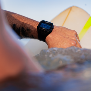 Wearing a Freestyle SHARK CLASSIC TIDE 600 BLACK, a surfer checks tide times while paddling on a board.