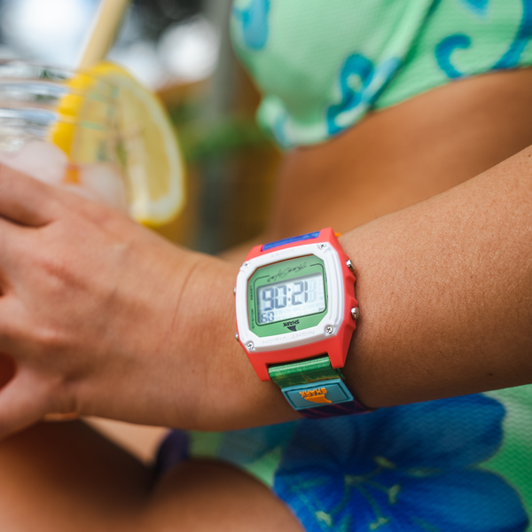 Individual wears a Freestyle Shark Classic Clip watch with a tie-dye design in green and neon, sipping a lemon drink while dressed in green and blue clothing.