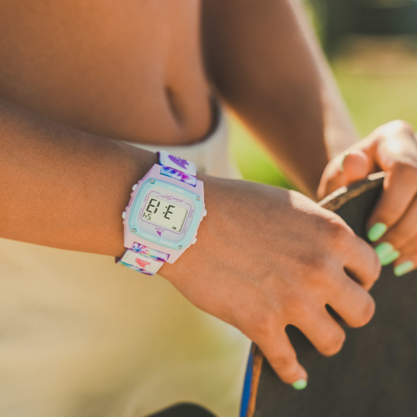 A person holding a skateboard is wearing a Freestyle Shark Classic Clip Snow Cone watch, with green nail polish visible on their fingers.