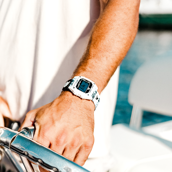 Wearing a white Freestyle SHARK CLASSIC CLIP BULLSEYE watch, a person holds a metal railing outdoors under bright sunlight.