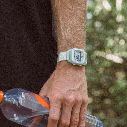 Wearing a Freestyle SHARK CLASSIC CLIP LIME, a person holds a water bottle outdoors with vibrant green foliage in the background.