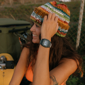 Smiling woman in a knit hat displays her Freestyle SHARK CLASSIC CLIP GRANITE PEAK watch while sitting beside a skateboard.