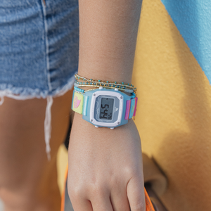 A person wearing a Freestyle SHARK CLASSIC LEASH SLUSHY watch and beaded bracelets, standing outdoors in shorts.