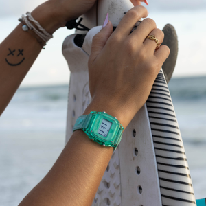 Wearing a Freestyle SHARK CLASSIC CLIP KIWI, someone stands at the beach holding a striped surfboard and showing off a smiley tattoo.