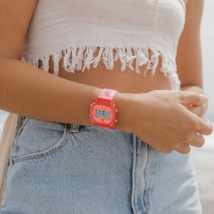 A person in light denim shorts, a fringed white top, and a Freestyle SHARK CLASSIC CLIP CHERRY watch clasps their hands.