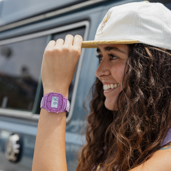 Smiling person wearing a SHARK CLASSIC CLIP PLUM watch and cap standing beside a blue vehicle.