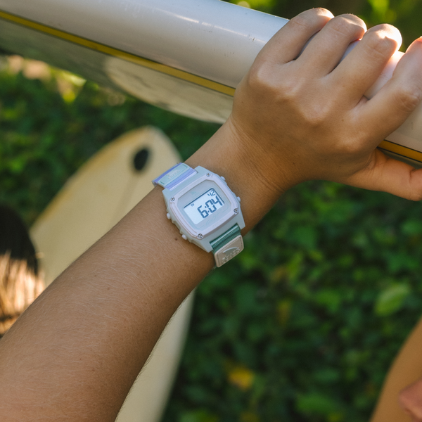 Close-up of a wrist wearing the Freestyle SHARK CLASSIC LEASH - ARCTIC RUSH, holding a surfboard outside.