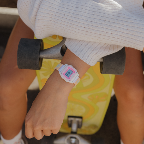 Person wearing a Freestyle SHARK MINI LEASH watch in blue tie-dye design, resting on a yellow skateboard.