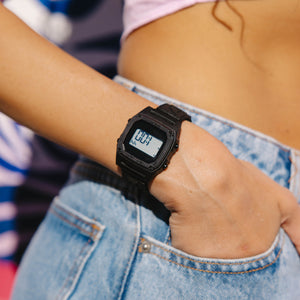 Person wearing a black digital watch on a blurred background