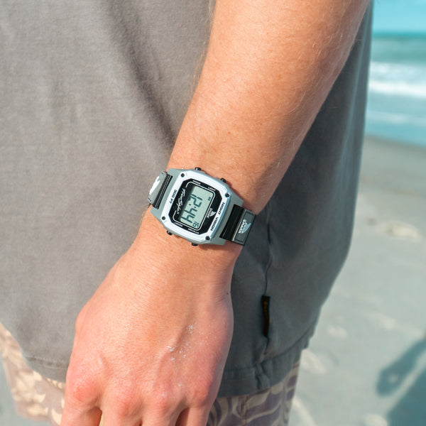 Grey and black digital watch on a wrist with a beach background
