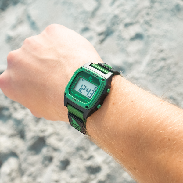 Green digital watch on a wrist with a blurred beach background