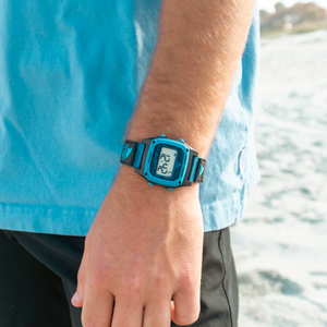 Person wearing a black and blue digital watch with a beach background