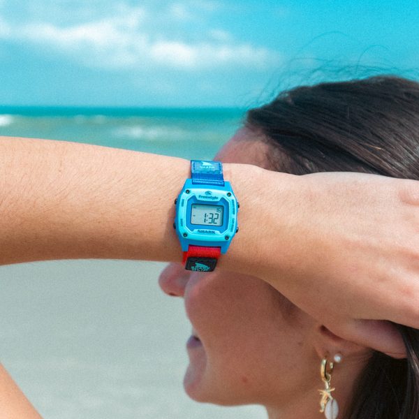 Person wearing a blue digital watch with a beach in the background