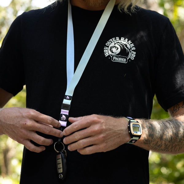 A person in a black shirt wears a Freestyle Lanyard and Key Chain in Green Tea color, standing outdoors with blurred trees in the background.