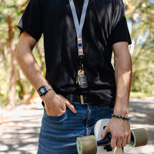 Person in black tee and jeans holding a skateboard, wearing a Freestyle Sahara Lanyard & Key Chain and a Shark Watch.