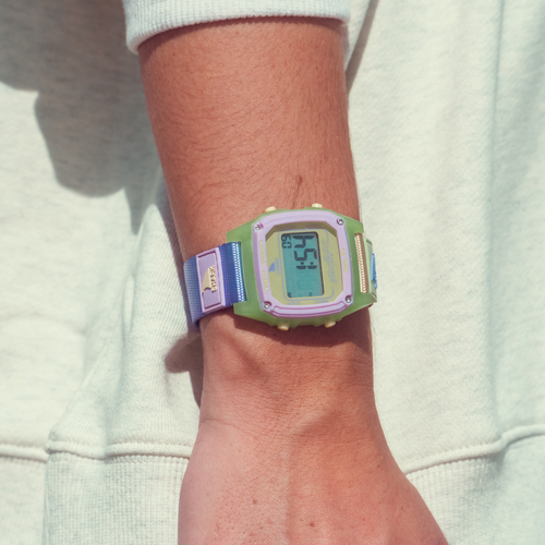 Person wears a Freestyle SHARK CLASSIC CLIP HONEY POP surf watch with a pastel strap and green-purple face, display lit up.