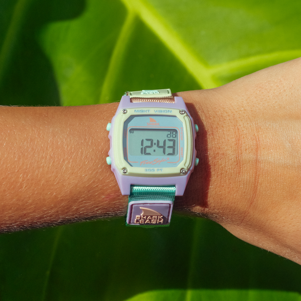 A SHARK CLASSIC LEASH MINT POP Freestyle watch is worn on a wrist against a green leaf background.