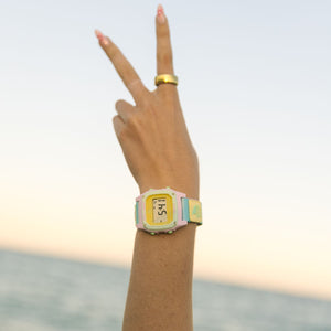 Hand showing a peace sign wearing the Freestyle SHARK CLASSIC CLIP SCENIC SKY watch, with ocean and sky in the background.