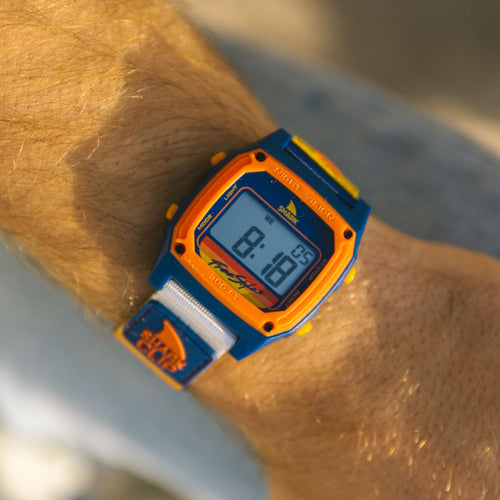 A close-up of a person wearing the Freestyle SHARK CLASSIC CLIP SURF CITY watch featuring blue and orange accents.