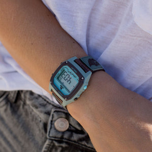 A person wearing a Freestyle SHARK CLASSIC CLIP GREY/BLUE watch, paired with a white shirt and gray jeans.
