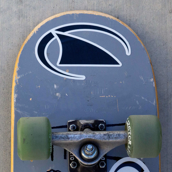 Gray skateboard with green wheels, worn deck, and Freestyle Fin Waterproof Decal by Freestyle, resting on concrete surface.