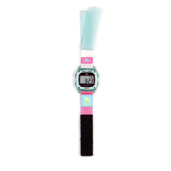 The CAROLINE MARKS SIGNATURE SHARK CLASSIC LEASH CLEAR BLUE SKY by Freestyle is a retro digital wristwatch featuring pastel mint green, pink, and blue tones. It has an adjustable Velcro strap displaying 3:23, adorned with a bird graphic and text inspired by Caroline Marks.