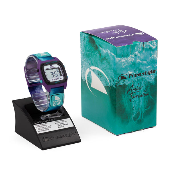 AMBER TORREALBA SIGNATURE SHARK CLASSIC CLIP REFLECTION with a purple and turquoise frame and silver lens next to its turquoise box.