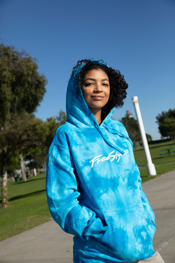 Smiling woman wears a Freestyle Unisex Aqua Dream Hoodie outdoors in a bright, green park.