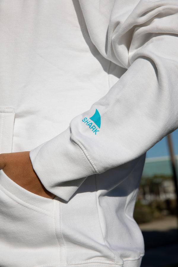 Person in comfy Unisex Neon Dream Logo Hoodie by Freestyle, hand in pocket, 80s blue shark fin on sleeve.